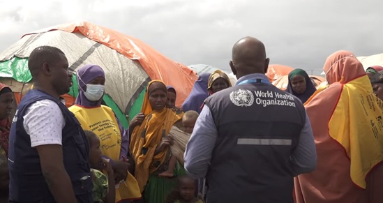 Two staff members of WHO talking to a group of women in a refugee camp